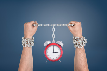 Two male hands bound together with chains and linked to a red retro clock.