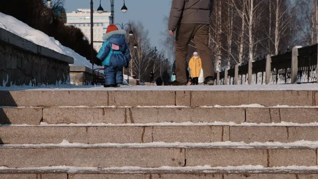 Unrecognizable child walks in winter Park with his father next to snowy staircase.