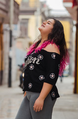 Lifestyle portrait of a beautiful young plus size woman smiling at camera in the city street.