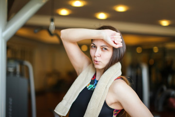 Close up portrait of adorable charming smiling young fitness girl with towel and posing while looking at camera in gym