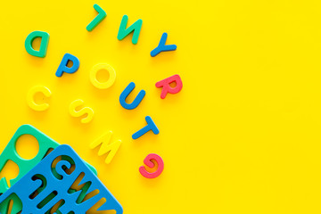 Alphabet for kids concept. English letters in disorder near stencil on yellow background top view copy space