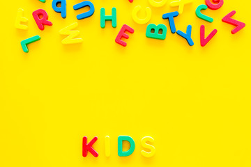 Early childhood development concept. Word kids written by plastic letters of toy alphabet on yellow background top view copy space