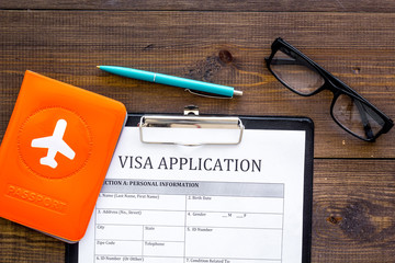 Visa processing, registration. Visa application form near passport cover with airplane on dark...