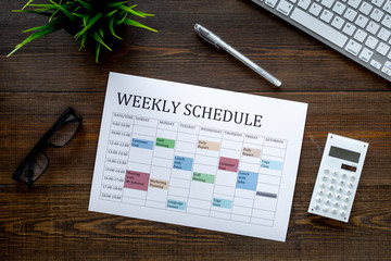 Weekly schedule. Planning the week. Multicolored planner on manager, marketologist's dark wooden...