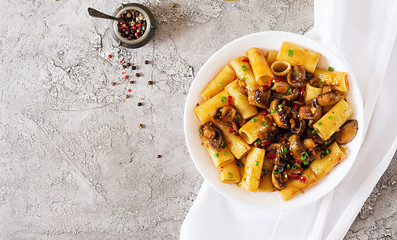 Vegetarian pasta  rigatoni with mushrooms and chilli peppers in white bowl on grey table. Vegan food. Flat lay. Top view