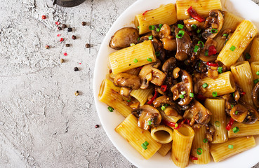 Vegetarian pasta  rigatoni with mushrooms and chilli peppers in white bowl on grey table. Vegan food. Flat lay. Top view