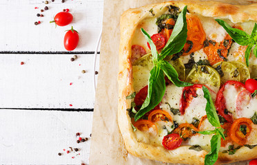 Mozzarella, tomatoes, basil savory pie on a white wooden background. Delicious food, appetizer in a mediterranean style. Top view. Flat lay