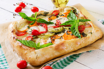 Mozzarella, tomatoes, basil savory pie on a white wooden background. Delicious food, appetizer in a mediterranean style.