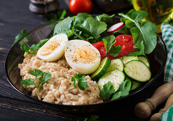 Healthy salad of fresh vegetables - tomatoes, cucumber, radish, egg, arugula and oatmeal on bowl. Diet food.