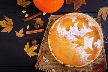 American homemade pumpkin pie with cinnamon and nutmeg, pumpkin seeds and autumn leaves on a wooden...