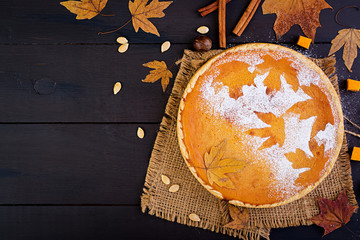 American homemade pumpkin pie with cinnamon and nutmeg, pumpkin seeds and autumn leaves on a wooden...