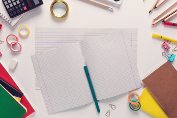Top view over a school supplies as calculator, rulers, tapes, paper clips, notebooks and other stuff placed in a circle on a white background with lined work book in the middle of it. Back to school c