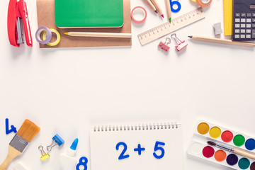 Top view over a notebooks, paints, pencils, rulers, paper clips, pins, calculator, glue, sharpener,...
