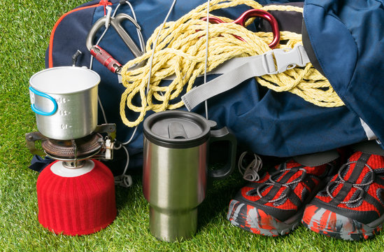 a tourist bag with shoes, on a green lawn, next to a red gas burner and a mug