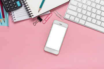 Top view office desk with empty smartphone, computer and office supplies on a pink background