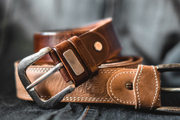 Two brown leather belts on dark background - obrazy, fototapety, plakaty