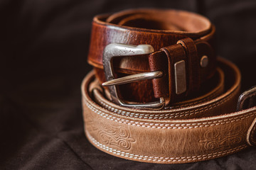 Two brown leather belts on dark background