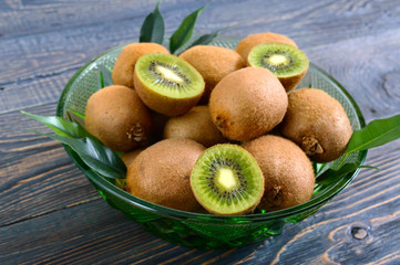 Ripe kiwi fruit in a green bowl on a wooden table.
