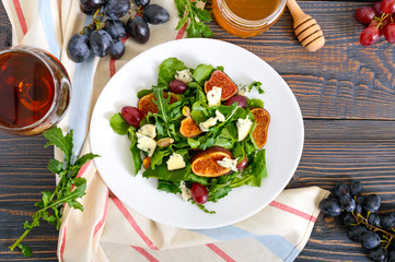 Classic salad with figs, arugula, blue cheese, grapes on a white plate on a wooden table. A delicious vegetarian dish.