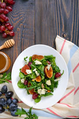 Classic salad with figs, arugula, blue cheese, grapes on a white plate on a wooden table. A delicious vegetarian dish.