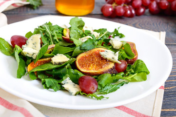Classic salad with figs, arugula, blue cheese, grapes on a white plate on a wooden table. A delicious vegetarian dish.