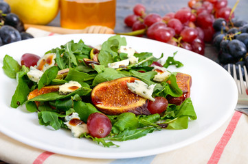 Classic salad with figs, arugula, blue cheese, grapes on a white plate on a wooden table. A delicious vegetarian dish.