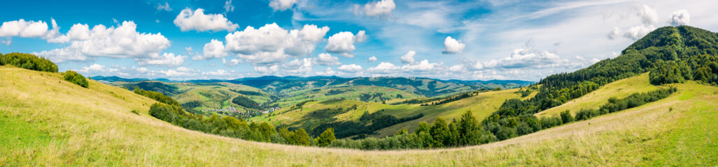 Fototapeta na wymiar panorama of beautiful autumn countryside. forest behind the meadow. gorgeous cloudscape on the sky above the distant hills. wonderful warm and sunny september day for a walk or hike