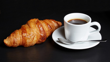  Cup of coffee with a croissant on a dark background.