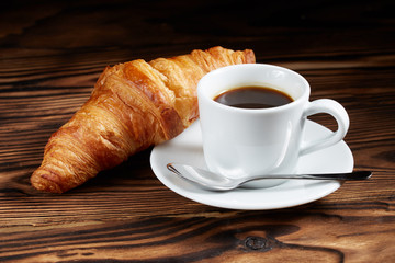 Cup of coffee with a croissant on a dark wooden background.
