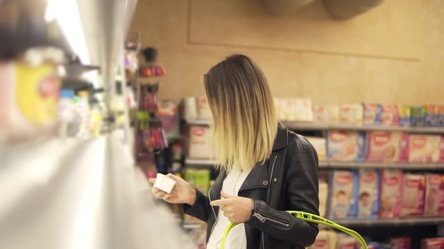 Woman chooses yogurt in the supermarket. Blonde smiling woman choosing products in shopping mall. Girl stands near the store shelf. Side view