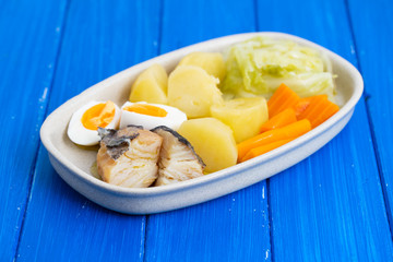 cod fish with boiled egg and vegetables on dish on blue background