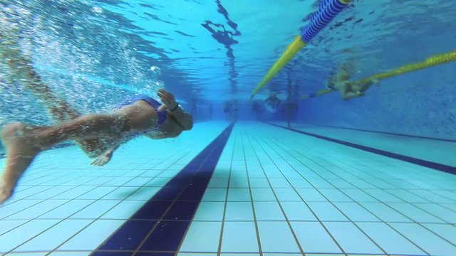 The teenager swims in the pool under the water.