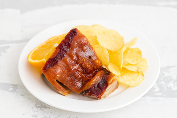 roasted piglet with potato chips and orange on white plate