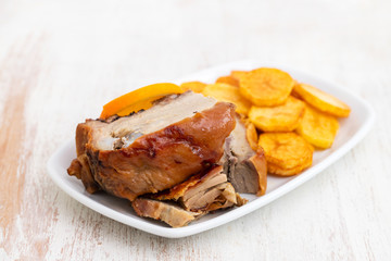 roasted piglet with potato chips and orange on white plate