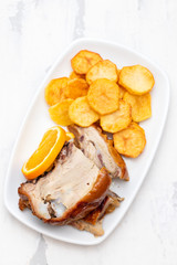 roasted piglet with potato chips and orange on white plate