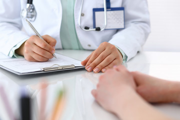 Doctor woman consulting patient while filling up an application form at the desk in hospital. Just hands close-up. Medicine and health care concept