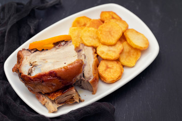 roasted piglet with potato chips and orange on white plate