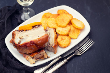 roasted piglet with potato chips and orange on white plate