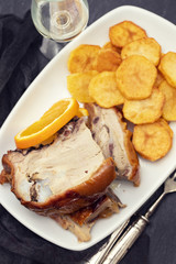 roasted piglet with potato chips and orange on white plate