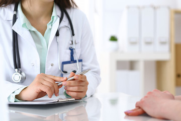 Doctor woman consulting patient while filling up an application form at the desk in hospital. Just hands close-up. Medicine and health care concept
