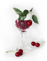  red cherry with green leaves and red beads in a glass on a white background 