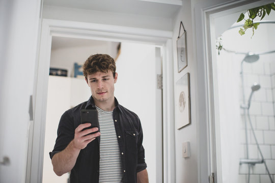 Young Adult Male Using Smartphone While Walking Through Home