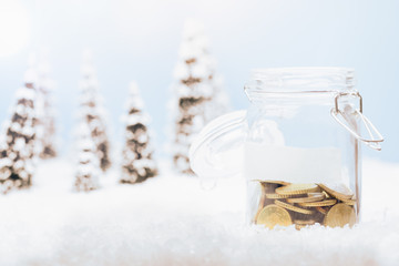 Half full money jar glass with coins for savings in Christmas holiday season background of snow landscape
