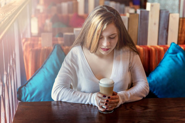 Beautiful teenage young smiling brunette girl sitting in cafe or bar and drinking latte macchiato ....