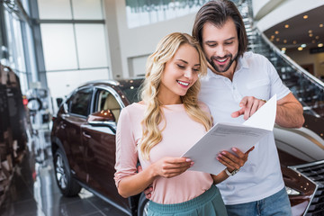 portrait of cheerful couple with catalog buying car at dealership salon