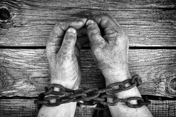Dirty male hands chained with old rusty thick chain on the wooden boards