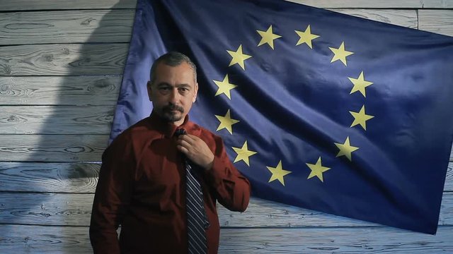 The politician straightens his tie in the background of the EU flag