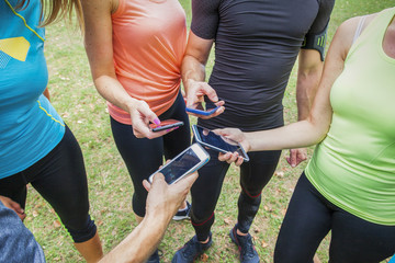 closeup of a group of sportsmen and sportswomen comparing their results on their mobile phones with sport apps outdoor in the city park
