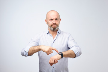 Mature european businessman impatiently pointing to his watch. Why are you late concept. - obrazy, fototapety, plakaty