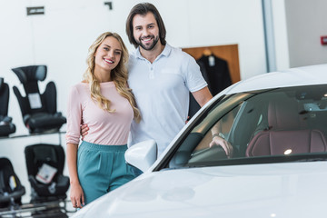 portrait of happy couple hugging at new car at dealership salon